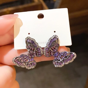 Detail of silver needle stud earrings with purple butterfly design and shimmering crystals