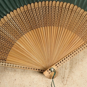 Bamboo silk folding fan with green fabric, intricate carved patterns and a matching tassel