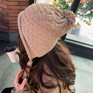 Close-up of khaki knitted beanie featuring textured geometric patterns and long tassels