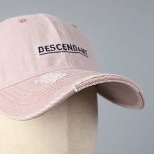 Close-up of pink distressed baseball cap with embroidered lettering and frayed edges