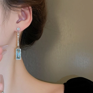 Close-up of model wearing geometric silver earrings with blue stones and diamonds
