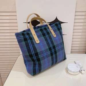 Detailed texture of blue and green plaid fabric on a tote bag with leather strap