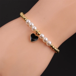 Close-up of beaded bracelet featuring gold beads, white pearls and a black heart charm