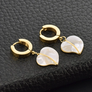 Elegant gold hoop earrings featuring heart-shaped shell pendants on black leather background