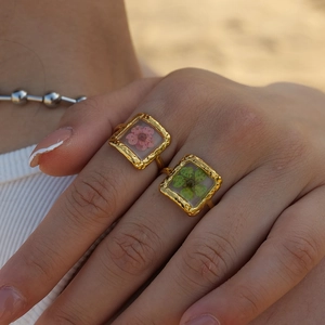 Detailed view of handmade gold rings with real pink and green dried flowers in square frames