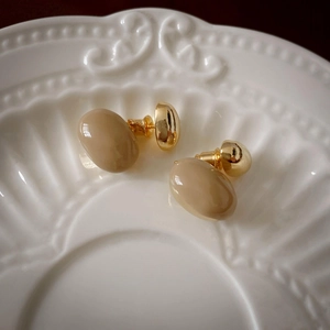 Detail view of irregular bean stud earrings in cream resin and gold on a ceramic tray