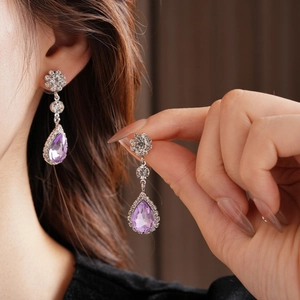 Macro shot of silver-toned drop earrings with purple crystals and sparkling floral accents