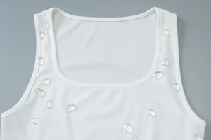 Dettaglio di abito in maglia a coste bianca con decorazione di perle a goccia sul collo