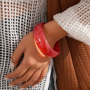 Detailed view of chunky resin bangle with deep red marble texture on woman's wrist