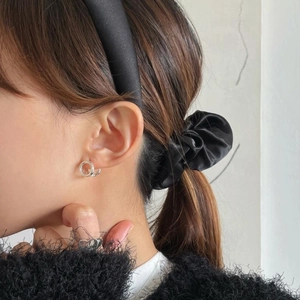 Detail of silver double-loop hoop earrings and a black satin headband on a model