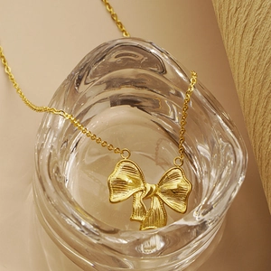 Elegant gold bow pendant necklace for women displayed on a stylish glass rim