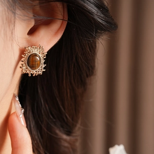 Close-up of gold metal earrings with brown tiger eye stones on female model's ear