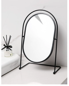 Detail of an oval desktop vanity mirror with a black metal frame and arch stand