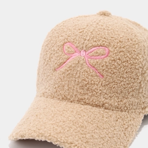 Detailed macro view of soft beige teddy faux fur texture and pink bow embroidery on cap
