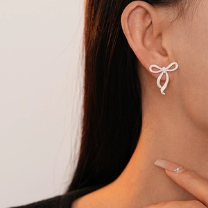 Macro view of a white lacquer bow stud earring worn by a female model