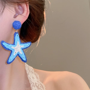 Model wearing blue and white raffia woven starfish earrings for a beach vacation look