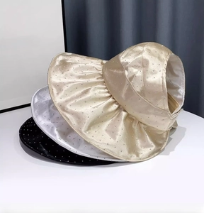 Detailed view of satin sun visors in black and gold with rhinestone accents and wide brims