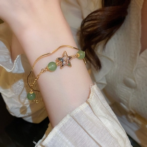 Close-up of double-layer gold bracelet with green beads and iridescent star pendant