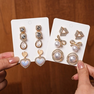 Close-up of gold stud earrings set featuring rhinestones, pearls and heart designs