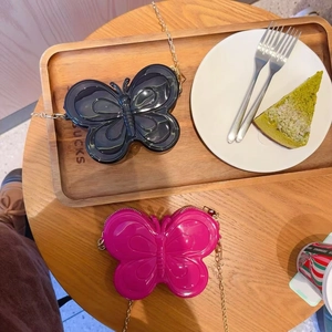 Détail de sacs bandoulière papillon en gelée avec chaînes dorées sur table en bois