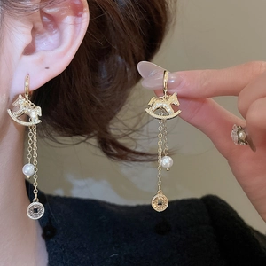 Détail de boucles d'oreilles cheval à bascule doré avec pompons, perles et pièces