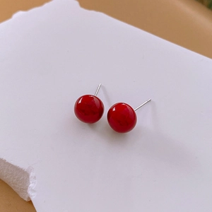Macro detail of glossy red spherical stud earrings with silver needles on stone