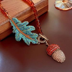 Macro detail of vintage leaf and acorn pendants set with vibrant crystals on beaded chain