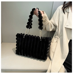 Detail of black fuzzy tote bag with striped texture and golden chain strap on a sofa