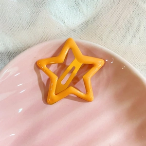 Close-up of a bright orange star-shaped drip oil hair clip on a pink ceramic dish