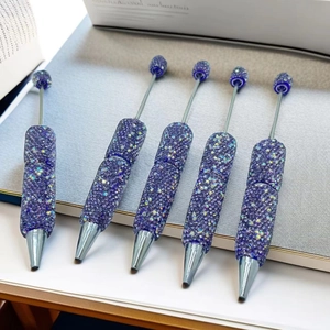 Set of five purple glitter rhinestone pens with metallic tips on a minimalist desk