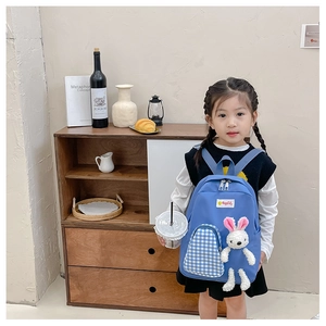 Blue toddler backpack with cute bunny plush toy shown on child model in soft indoor lighting