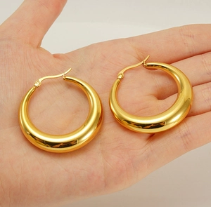 Macro detail of thick 18K gold plated hollow hoop earrings held in hand for scale