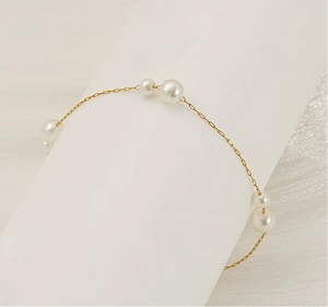 Detailed close-up of a gold pearl bracelet on a minimalist white display stand