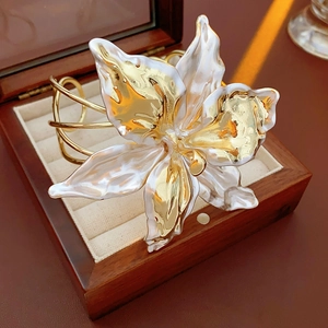 Macro shot of large lily flower cutout open bracelet with pearlescent finish on gold metal