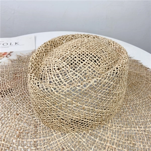 Detailed macro view showing the textured natural seagrass weave and fringe of the sun hat