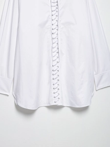 Detail of white long sleeve blouse featuring front lace-up design with silver metal eyelets