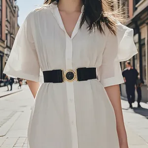 Women's black elastic waist belt with a golden round buckle on a white shirt dress