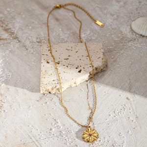 Detailed shot of gold sunflower pendant with pink gemstone on stone and shell background