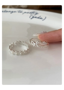 Macro detail of adjustable silver bow ring and floral pearl ring on a ceramic plate