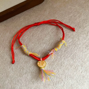 Gros plan du bracelet tressé rouge avec pendentif coeur doré et caractère Fu chinois