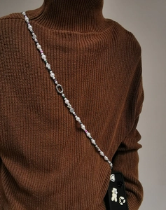 Detail of beaded crossbody phone chain with pearls and floral charms on a sweater