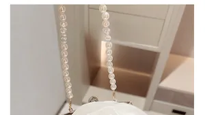 Detailaufnahme der elfenbeinfarbenen Abendtasche mit 3D-Blumen und Perlenkette-Riemen