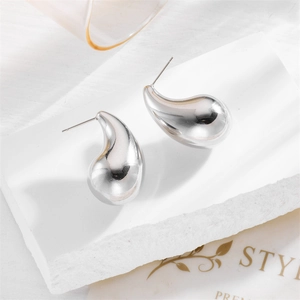 Polished silver teardrop earrings with minimalist geometric design on a white stone