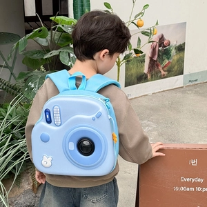 Zainetto rigido azzurro a forma di fotocamera indossato da un bambino in un giardino
