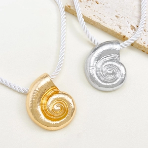 Vintage gold and silver conch shell pendant necklaces with woven cords on stone display