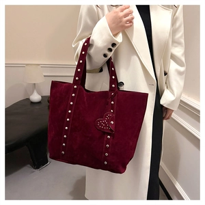 Detail of burgundy suede tote bag featuring heart charm and metal rivet accents