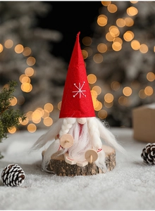 Detail of Christmas gnome figurine with felt hat on a rustic wood log with snowy bokeh background