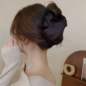 Detail of a large black satin bow hair claw clip with crystal edges on a model