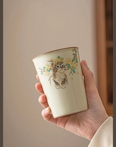 Close-up of handmade celadon tea cup with a cute cat illustration and cracked glaze finish
