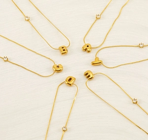 Detail of gold bubble initial necklaces with zircon stones on soft textured fabric